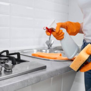 Mujer con guantes amarillos utilizando consejos profesionales para limpiar muebles de cocina blancos.